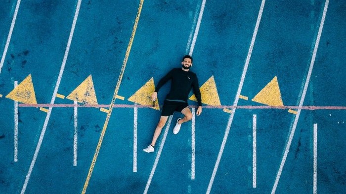 Eine Person, die auf einer blauen, gestreiften Stadtstraße mit gelben dreieckigen Markierungen Skateboard fährt.