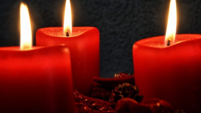 Drei brennende rote Kerzen vor dunklem Hintergrund