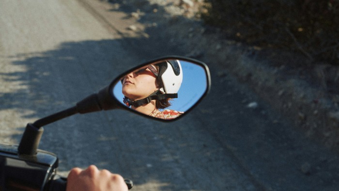 Eine  Fahrrad- oder Mopedfahrerin schaut beim Fahren in den Rückspiegel