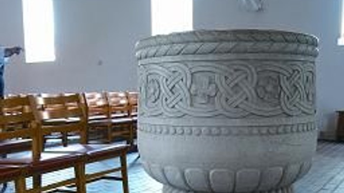 En smukt, grovsnitret font i en kirke med træbænke.