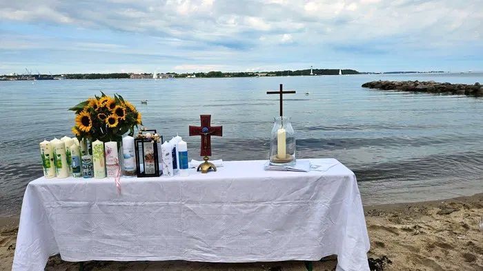 Ein Tisch am Strand mit Blumen, Kerzen und Kreuzen