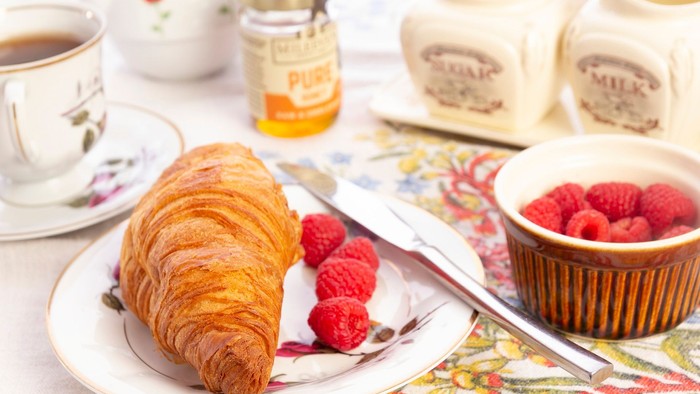 Ein Frühstücksbild mit Croissant, Himbeeren, Tee und Marmelade