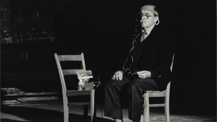 Alter Mann sitzt auf Stuhl, raucht Pfeife, trägt Anzug und Brille