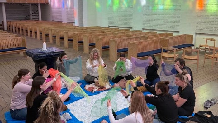En gruppe unge sidder på yoger i en kirke og ser en projeksjon.