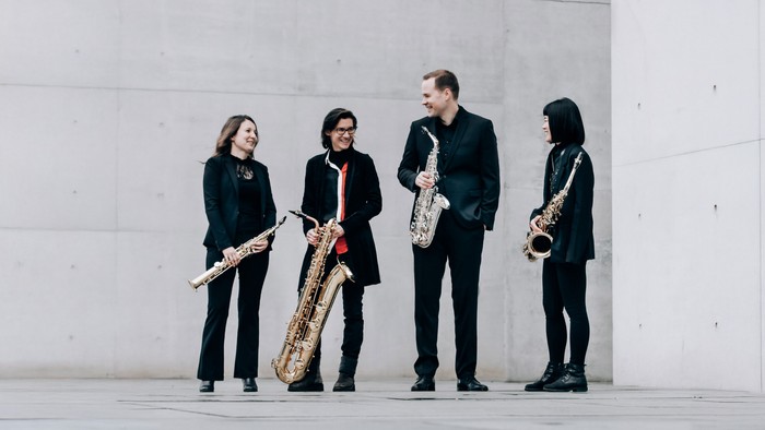 Vier Musiker posieren mit ihren Saxophonen vor einer Betonwand