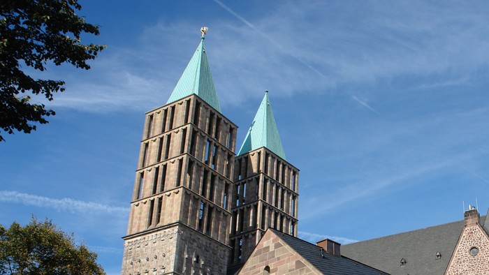 Große Kirche mit Zwillingstürmen und einem Kreuz obenauf, umgeben von Bäumen und Gebäuden.