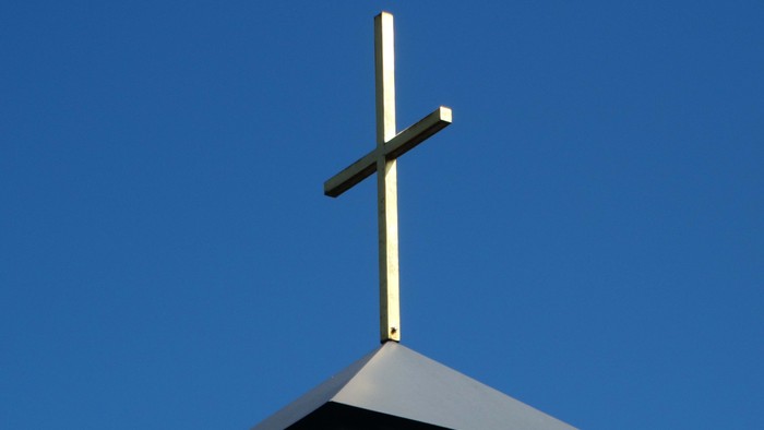 Ein Kreuz steht auf einem Dach vor blauem Himmel.