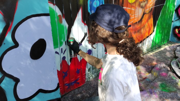 Ein Kind mit einer blauen Mütze sprüht eine bunte Wand.