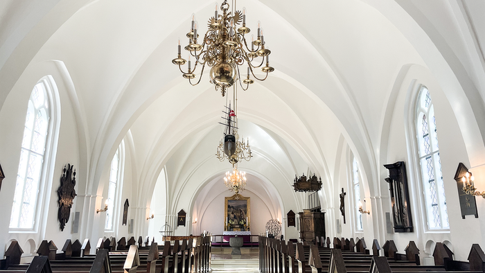 Indenrigspart af en stor, belyset kirke med høje buer og centrale lys.