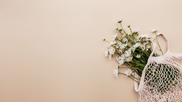 En hvid meshpose holder sarte hvide blomster mod en blød ferskenfarvet baggrund.