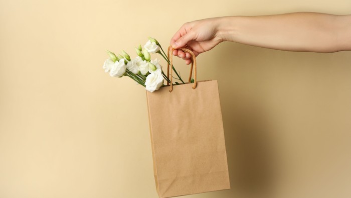En hånd holder en papirpose med hvide blomster.