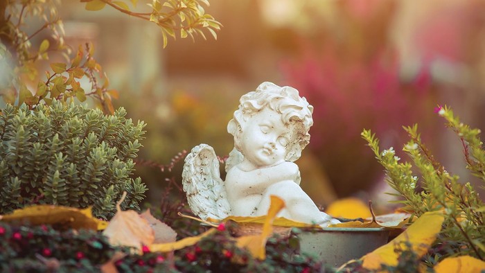 En lille, hvid marmorkyndel sidder i en plantekasse med blomster og løv.