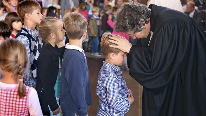 Ein Mann in schwarzer Robe segnet Kinder in einer Kirche.