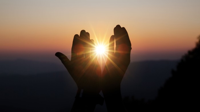 En person holder hænderne op mod solen ved solopgang eller solnedgang