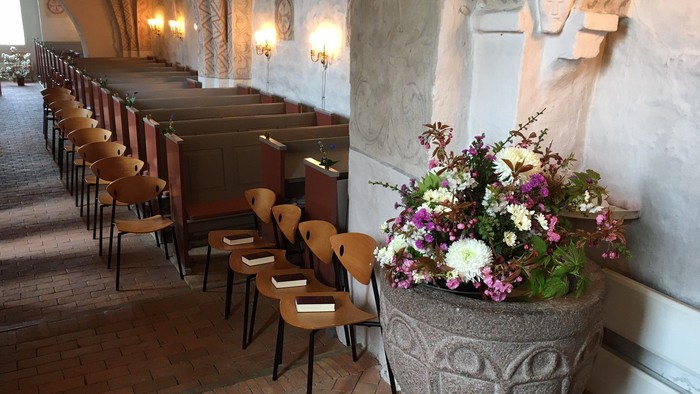 En kirkeinterior med træstoler og en stor blomsterpot på gulvet