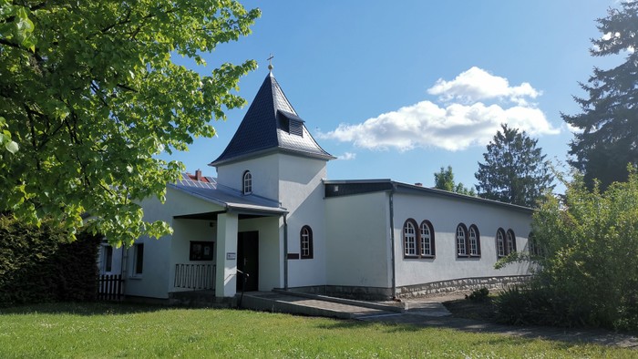Eine malerische weiße Kirche mit steilem Dach und Glockenturm in einer üppigen grünen Landschaft.