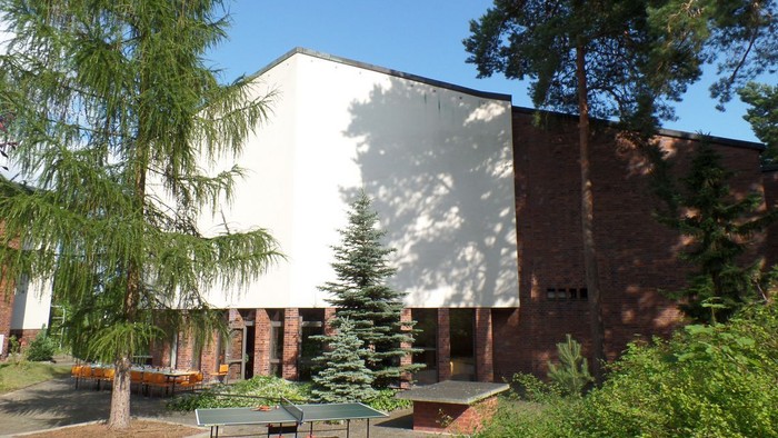 Das Bild zeigt ein Gebäude mit einem Innenhof, einem Tischtennisplatte und Bäumen.