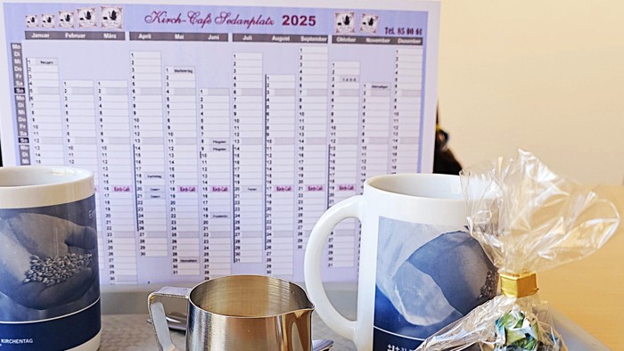 Ein Schreibtisch mit Kaffeetassen, Milchkännchen, Zuckerstücken und einem Korb mit Süßigkeiten vor einem Kalender.