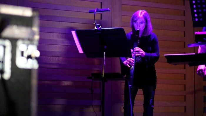 A woman sings into a microphone on stage with a music stand and keyboard.