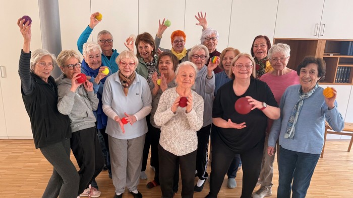 Gruppe älterer Menschen, die fröhlich an einer Gymnastikstunde mit bunten Bällen teilnehmen.