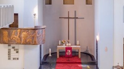 Kleine, helle Kirche mit Holzaltar und Kreuz, weißem Geländer und Rundfenstern.