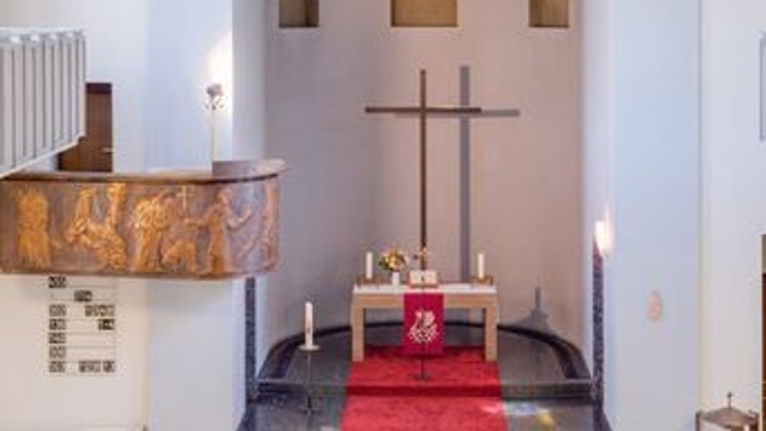 Kleine, helle Kirche mit Holzaltar und Kreuz, weißem Geländer und Rundfenstern.