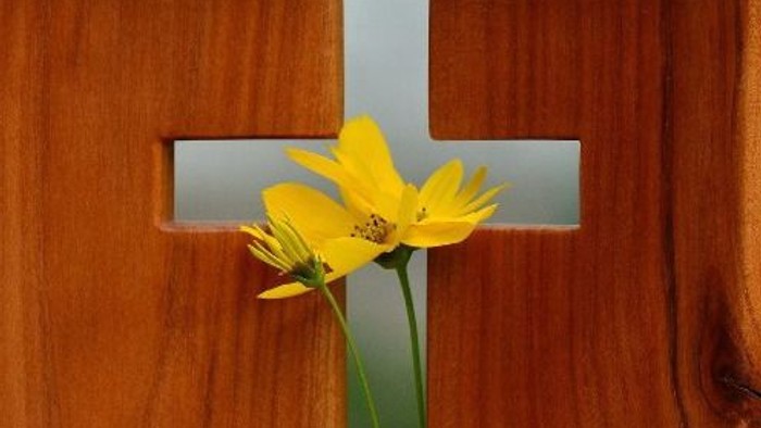 Ein gelber Blumenstrauß steckt in einem Kreuz aus Holz.