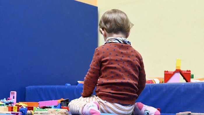 Ein kleines Kind sitzt auf dem Boden und spielt mit Bauklötzen.