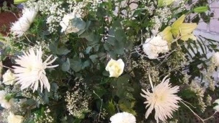 A bouquet of white flowers including chrysanthemums and baby's breath, accented with greenery.