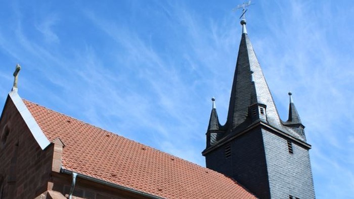 Kirche mit hohem Turmspitz und Bank davor.