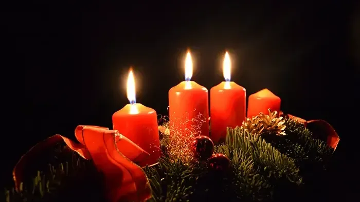 Vier brennende Kerzen auf Adventskranz mit Tannenzweigen und Nüssen