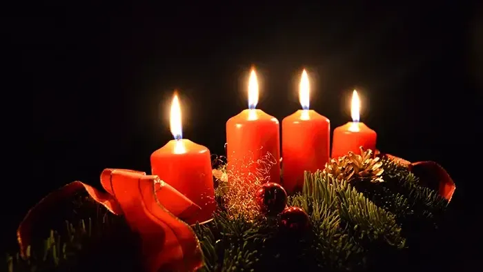 Vier brennende Kerzen auf Adventskranz im dunklen Raum