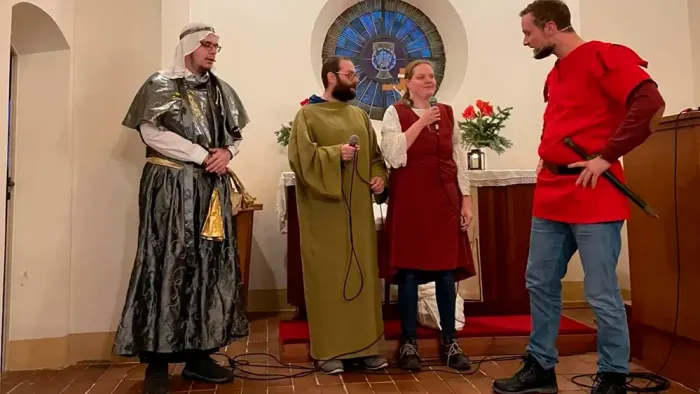 Vier Personen in historischen Kostümen stehen in einem Raum mit Kirchenfenster.