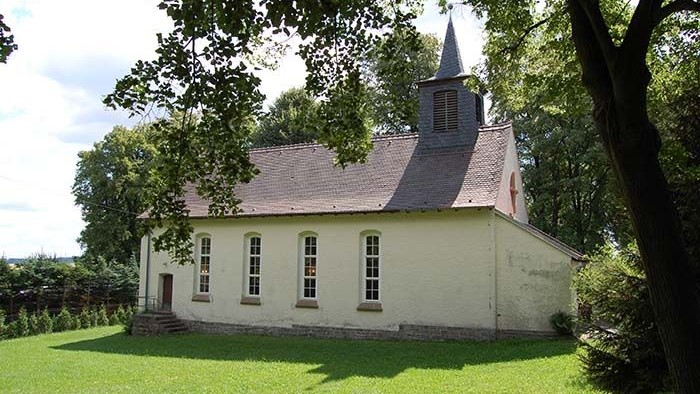 Kleine weiße Kirche mit Turm auf grünem Rasen unter Bäumen