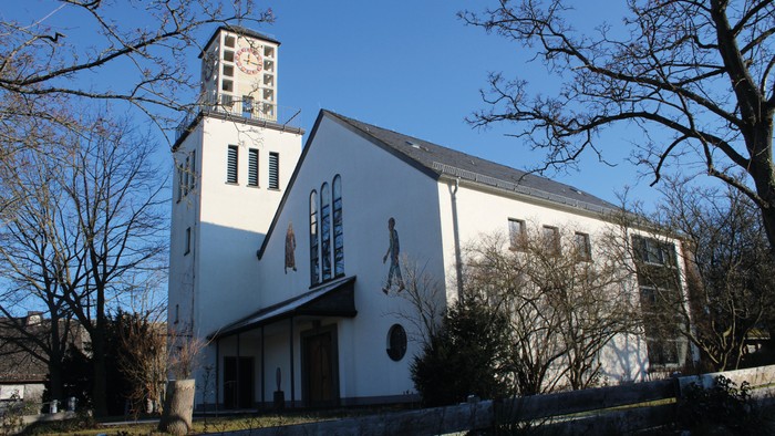 Weiße Kirche mit Turm und Uhr, umgeben von Bäumen und Himmel