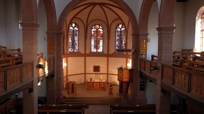 Elegante Kircheninnenausstattung mit hölzernen Kirchenbänken, Buntglasfenstern und einem zentralen Altarraum.