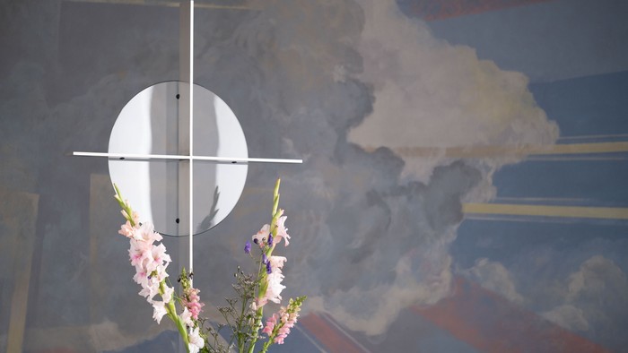 En blomstestok med blå og rosa blomster foran et maleri af himlen med en måne og skyer