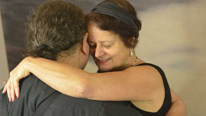 Zwei Frauen, die sich herzlich umarmen, eine mit einem Stirnband, beide lächelnd.