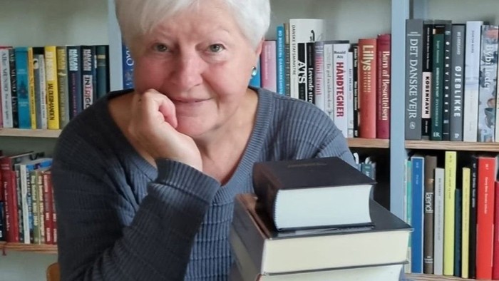 En person poser tankefuldt med en stak bøger i et hyggeligt, bogfyldt rum.