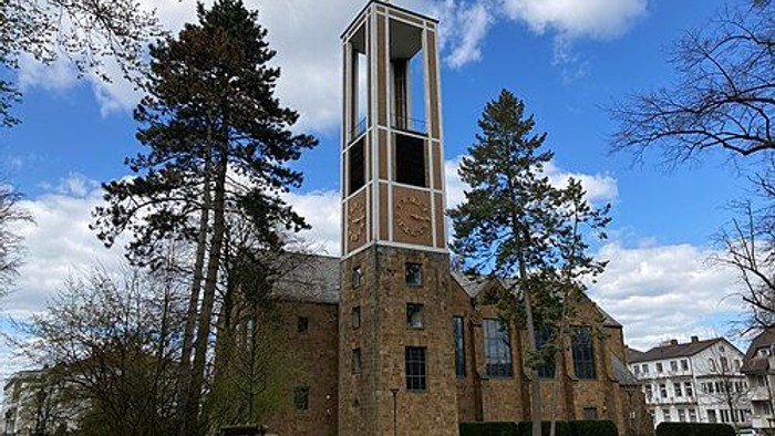 Eine Backsteinkirche mit einem hohen Glockenturm, umgeben von grünem Gras und hohen Bäumen.