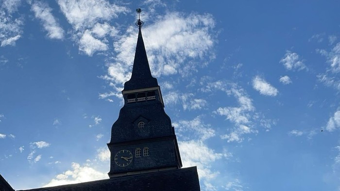 Kirchturm vor blauem Himmel mit weißen Wolken