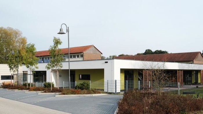 Modernes Gebäude mit großen Fenstern und umgeben von Bäumen und Büschen