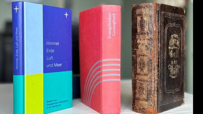 Drei Bücher in verschiedenen Farben und Bindungen stehen auf einem Tisch