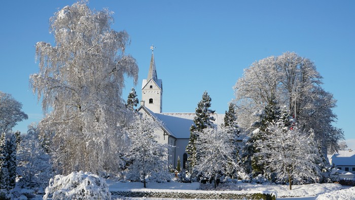 En snede kirke med tårn og nøgler, omgivet af snebede træer og en klar blå himmel
