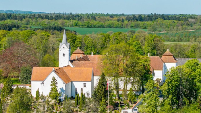 En lille landsby med kirke og huse omgivet af grønne skove og felter
