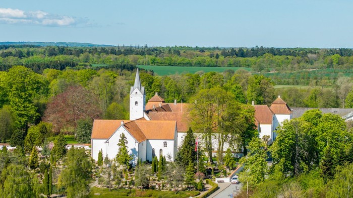 En lille landsby med kirke og huse omgivet af grønne skove og felter