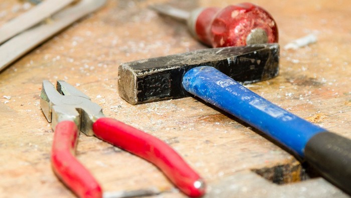 Ein Satz von Werkzeugen, einschließlich Zange und Hammer, liegt auf einem Holzarbeitsplatz