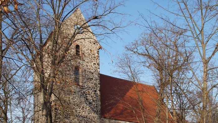 Alte Kirche mit Turm und rotem Dach, umgeben von kahlen Bäumen