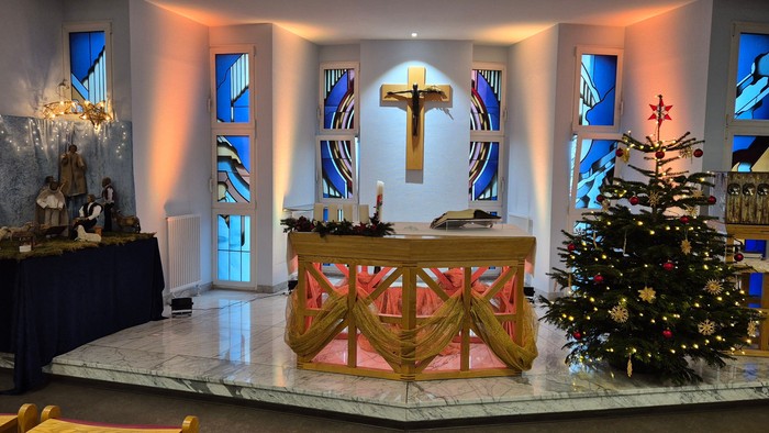 Kirchenaltar mit Weihnachtsdekoration, darunter ein Baum und eine Krippenszene.