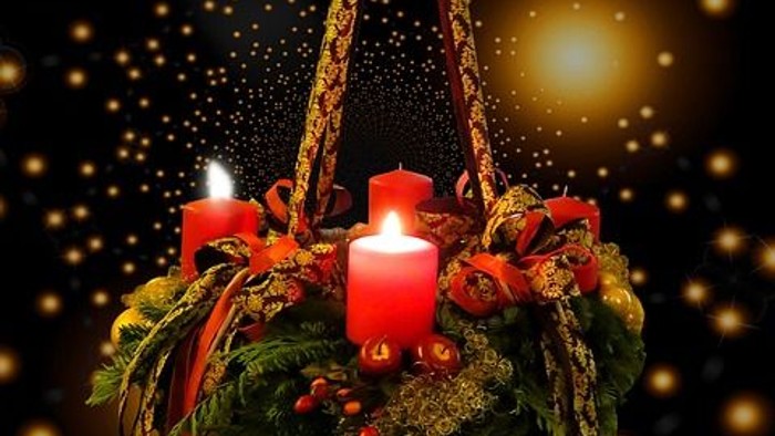 Ein Adventskranz mit vier brennenden Kerzen schwebt vor einem dunklen Hintergrund mit goldenen Sternen.